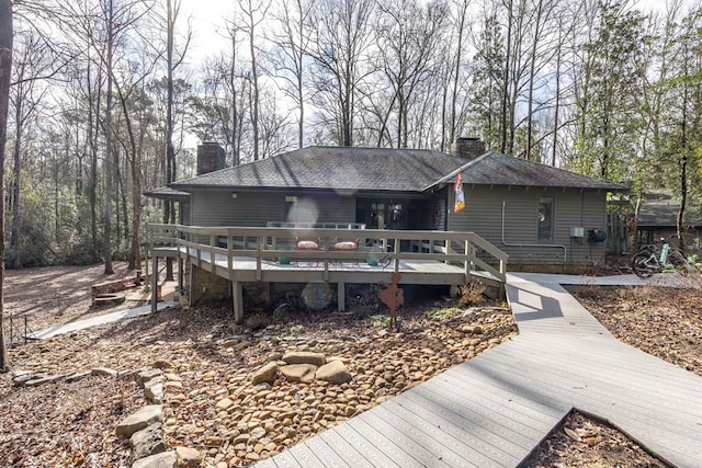 view of front of property featuring a chimney, a deck, and a shingled roof