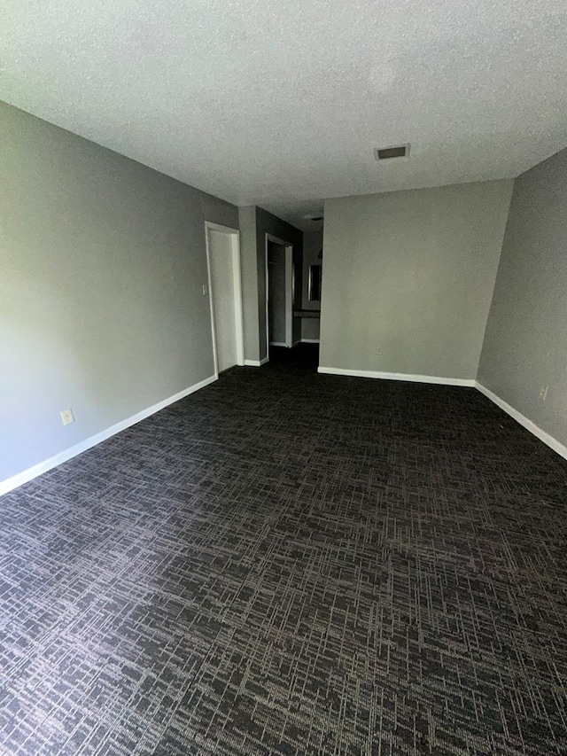 unfurnished room featuring dark colored carpet and a textured ceiling