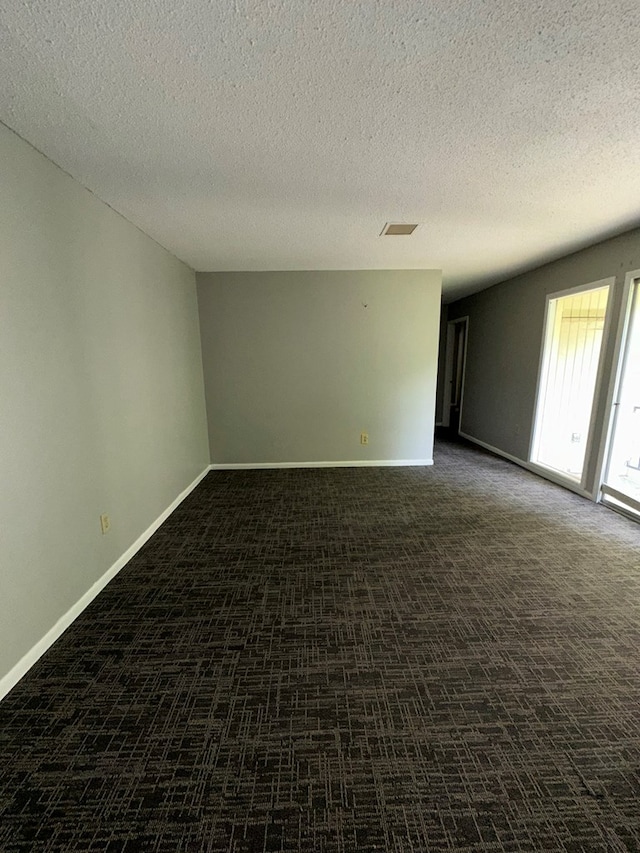 spare room with dark colored carpet and a textured ceiling