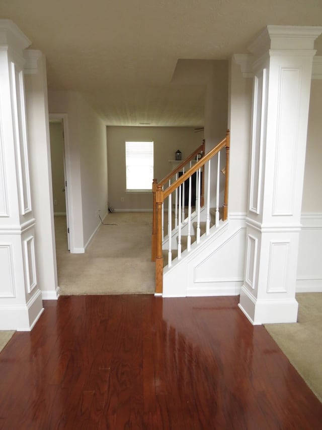 stairs with carpet floors, wood finished floors, a decorative wall, and decorative columns