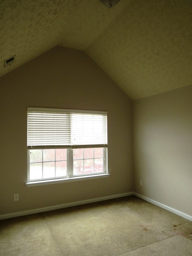 carpeted empty room featuring vaulted ceiling, baseboards, and a textured ceiling