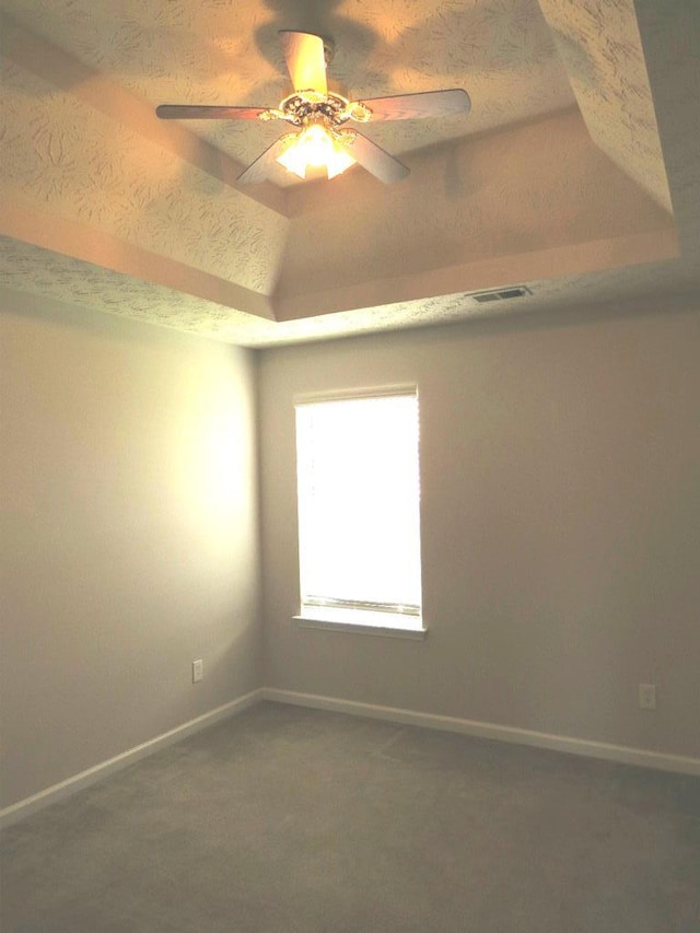 carpeted spare room with baseboards, a raised ceiling, visible vents, and ceiling fan