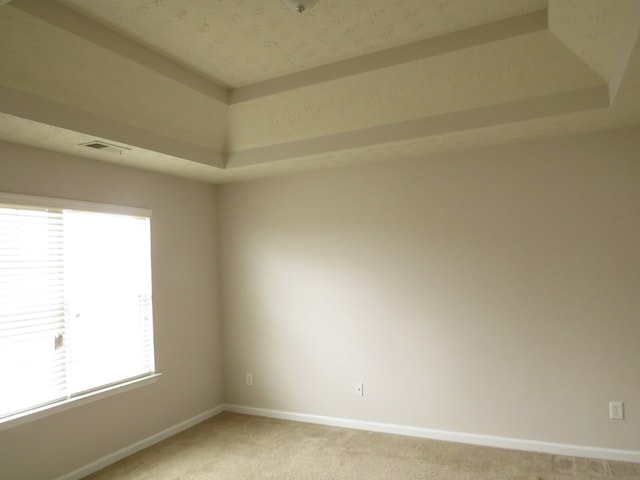 spare room with a tray ceiling, visible vents, baseboards, and light colored carpet