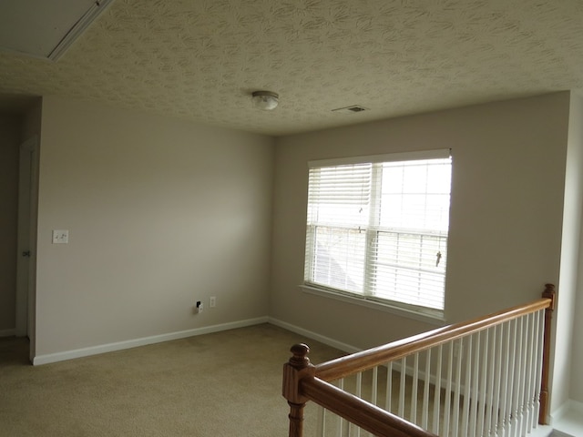 carpeted spare room featuring attic access, baseboards, visible vents, and a textured ceiling