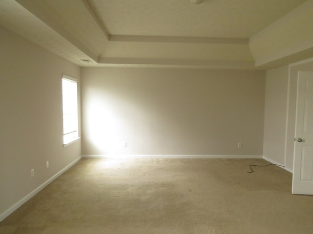 carpeted empty room featuring baseboards and a raised ceiling