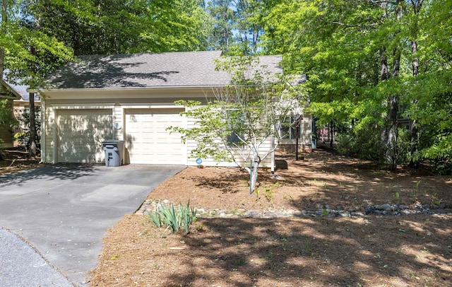 view of property hidden behind natural elements with driveway, roof with shingles, and a garage