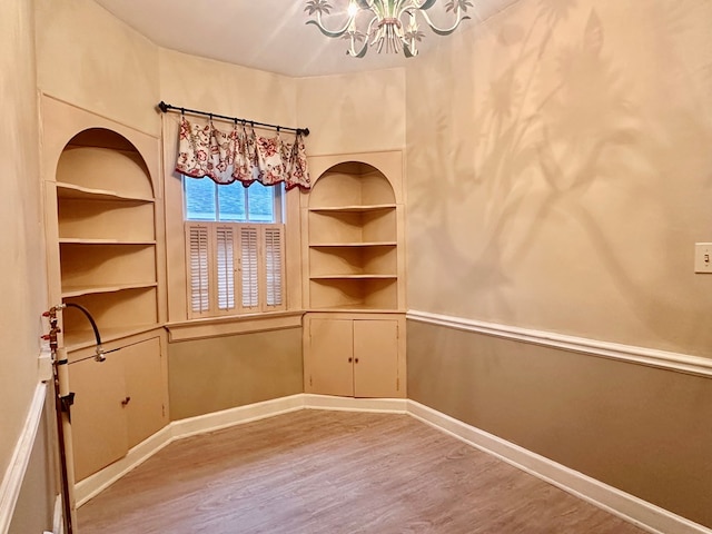 empty room with an inviting chandelier, hardwood / wood-style flooring, and built in shelves