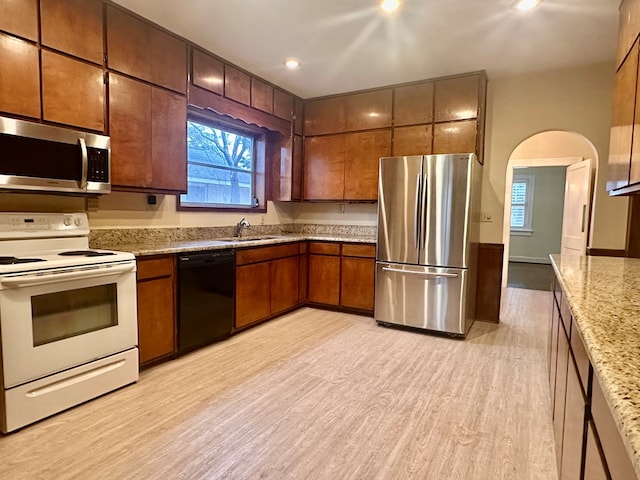 kitchen with light stone countertops, appliances with stainless steel finishes, sink, and light hardwood / wood-style flooring