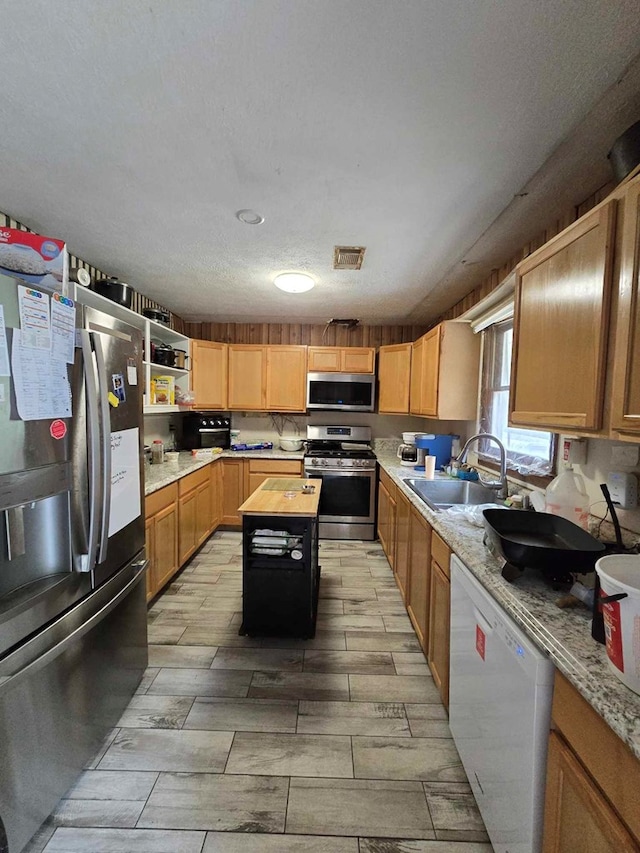 kitchen with sink, stainless steel appliances, light stone counters, a textured ceiling, and a kitchen island