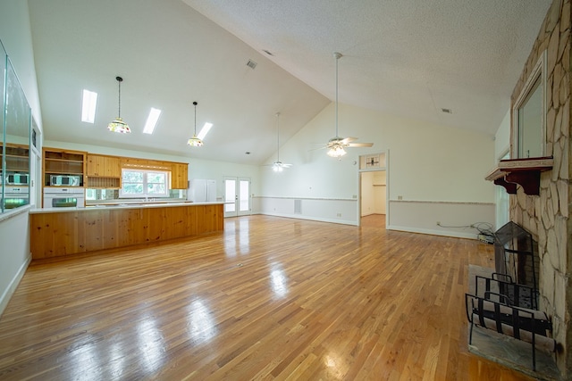 5604 Holland Dr, Columbus, GA 31909 - unfurnished living room featuring high vaulted ceiling, light wood finished floors, a skylight, ceiling fan, and a stone fireplace