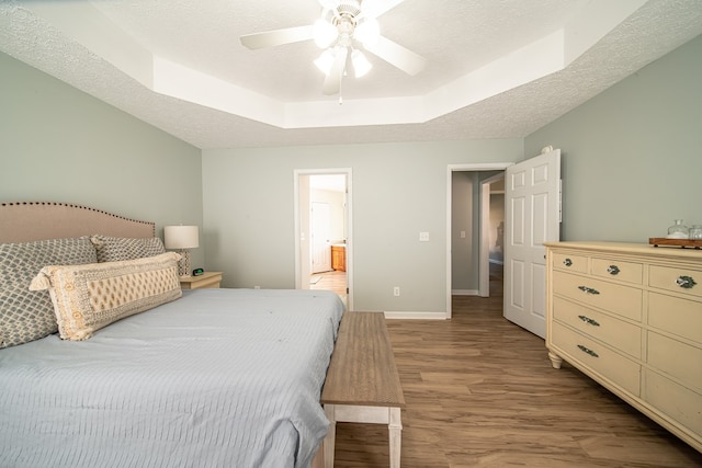 bedroom with ensuite bathroom, a textured ceiling, light wood-type flooring, a tray ceiling, and ceiling fan