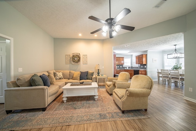 living room with hardwood / wood-style flooring, ceiling fan with notable chandelier, and a textured ceiling