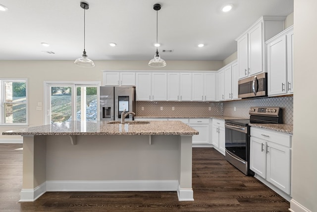 kitchen featuring stainless steel appliances, white cabinets, a kitchen island with sink, and hanging light fixtures