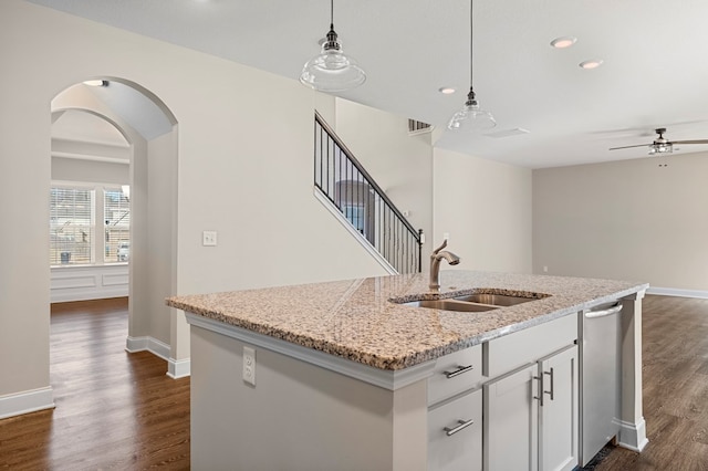 kitchen with an island with sink, light stone counters, sink, white cabinetry, and decorative light fixtures