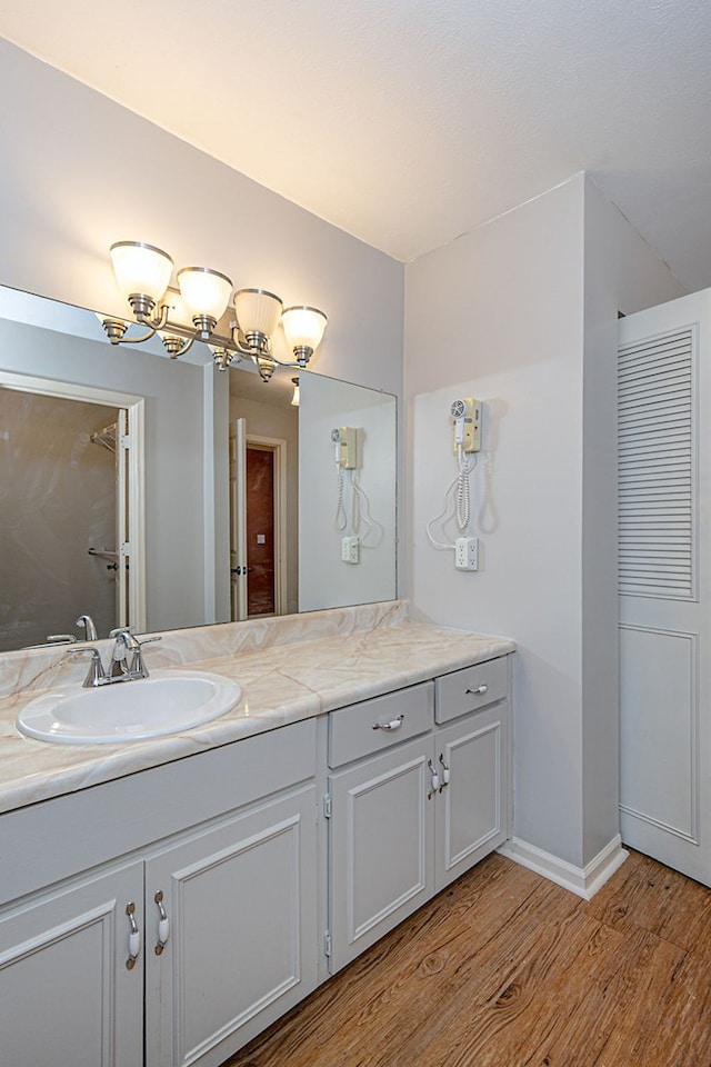 bathroom featuring an inviting chandelier, vanity, baseboards, and wood finished floors