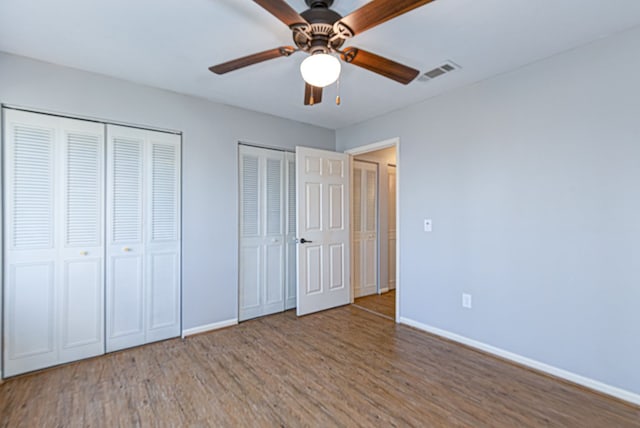 unfurnished bedroom with visible vents, baseboards, multiple closets, and wood finished floors