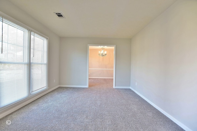 carpeted empty room featuring a chandelier, visible vents, and baseboards