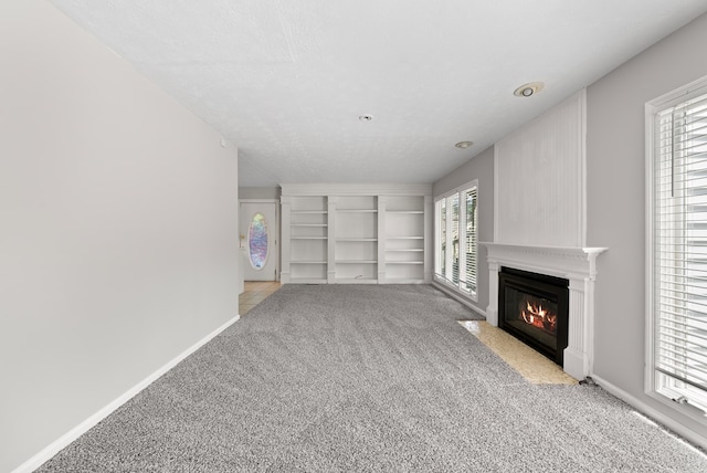 unfurnished living room featuring light carpet, a fireplace with flush hearth, built in shelves, and baseboards