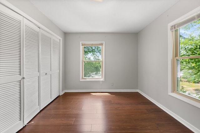 unfurnished bedroom with multiple windows, dark wood-type flooring, and baseboards