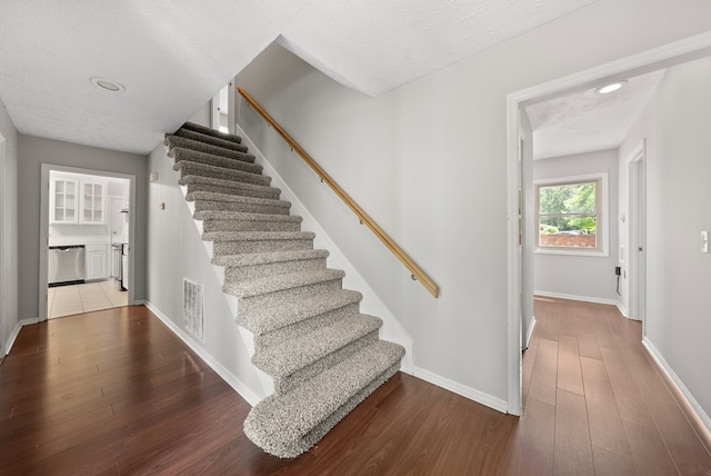 stairway featuring wood finished floors, baseboards, and a textured ceiling