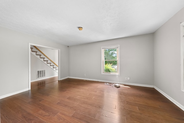 unfurnished room with stairs, wood finished floors, baseboards, and a textured ceiling