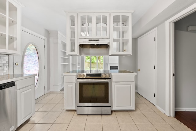 kitchen with appliances with stainless steel finishes, white cabinetry, under cabinet range hood, and glass insert cabinets