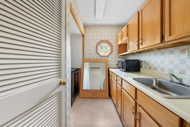 kitchen with black appliances, a sink, wallpapered walls, light countertops, and light tile patterned floors