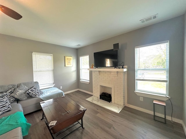 living room with a brick fireplace, wood finished floors, visible vents, and baseboards