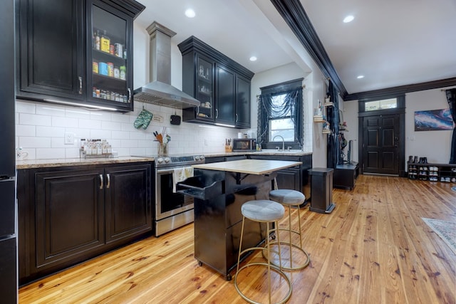 kitchen featuring wall chimney exhaust hood, a kitchen breakfast bar, a center island, crown molding, and stainless steel range with electric cooktop