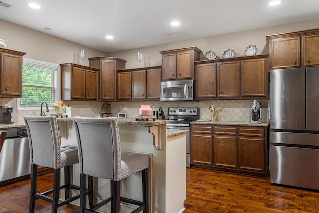 51 New Castle Dr, Phenix City, AL 36870 - kitchen featuring stainless steel appliances, dark wood-type flooring, a breakfast bar, light stone counters, and a center island