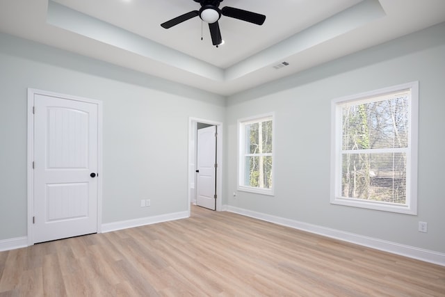 spare room with baseboards, a raised ceiling, and light wood-style flooring