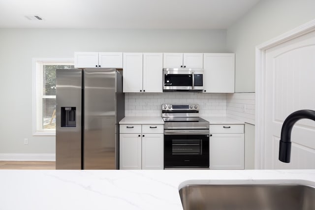 kitchen with light stone countertops, decorative backsplash, appliances with stainless steel finishes, white cabinetry, and a sink