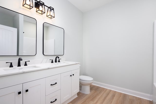 bathroom with toilet, wood finished floors, baseboards, and a sink