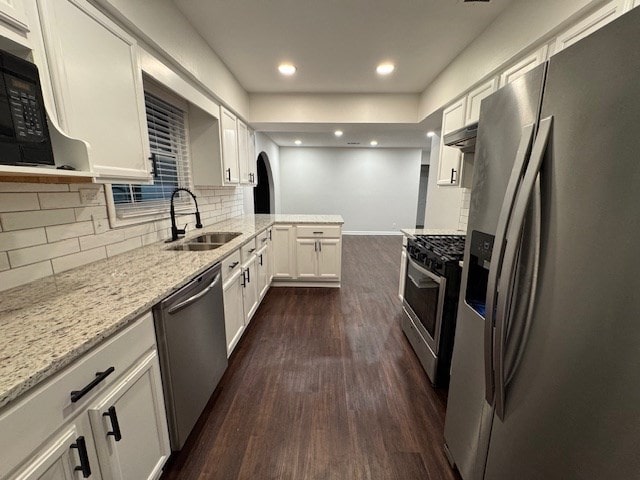 kitchen with light stone counters, dark wood-style floors, a sink, stainless steel appliances, and white cabinets