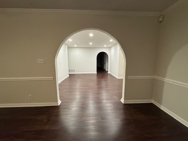 empty room featuring dark wood-type flooring, baseboards, and arched walkways