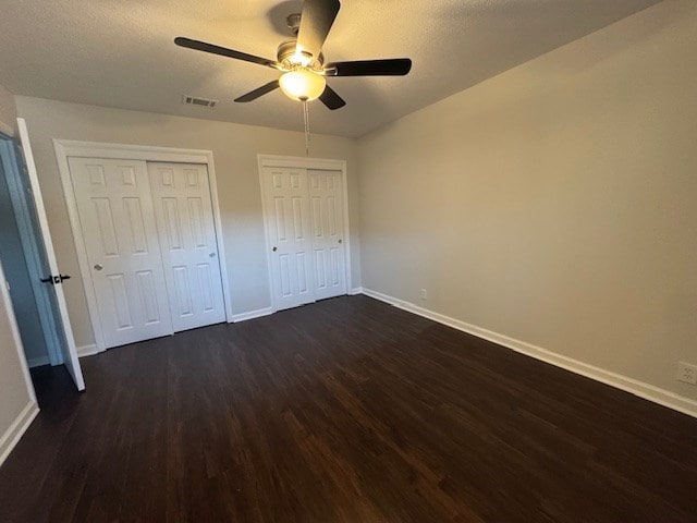 unfurnished bedroom with visible vents, dark wood-type flooring, ceiling fan, baseboards, and multiple closets