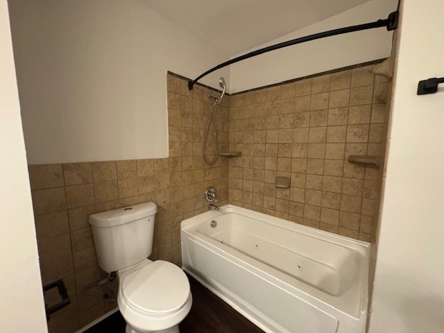 full bath featuring tile walls, toilet, a wainscoted wall, and shower / bath combination