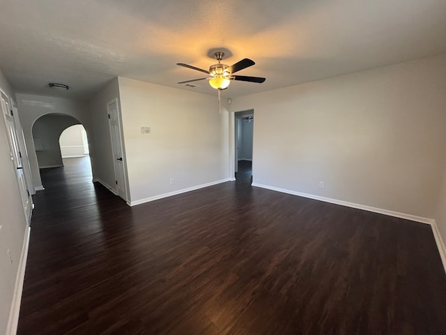 empty room featuring arched walkways, dark wood finished floors, baseboards, and a ceiling fan