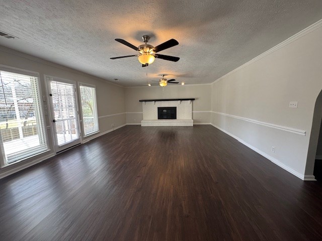 unfurnished living room with visible vents, crown molding, baseboards, a fireplace, and dark wood-style flooring