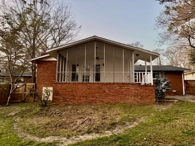 rear view of house with brick siding, a sunroom, and fence