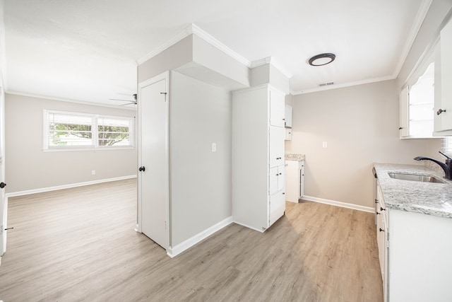 kitchen featuring a sink, ornamental molding, light wood-type flooring, white cabinetry, and baseboards