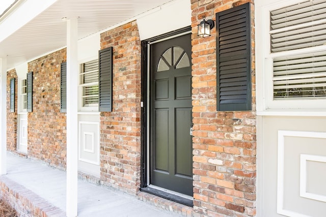 view of exterior entry with brick siding and covered porch
