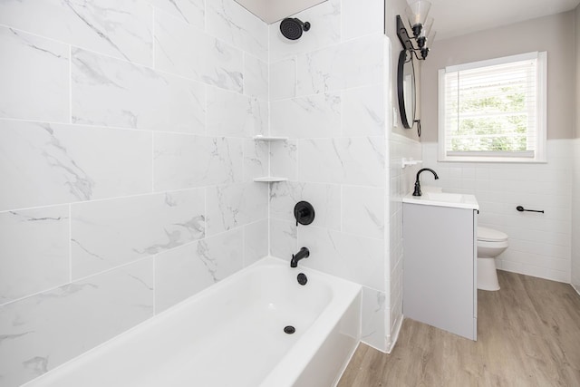 full bath featuring wood finished floors, toilet, shower / bath combination, tile walls, and a wainscoted wall