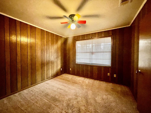 carpeted spare room with crown molding, wooden walls, a ceiling fan, and visible vents