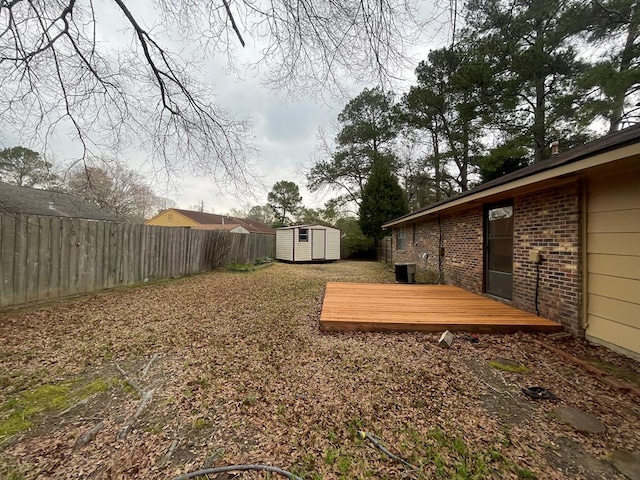 view of yard with a storage unit, a deck, an outbuilding, and a fenced backyard