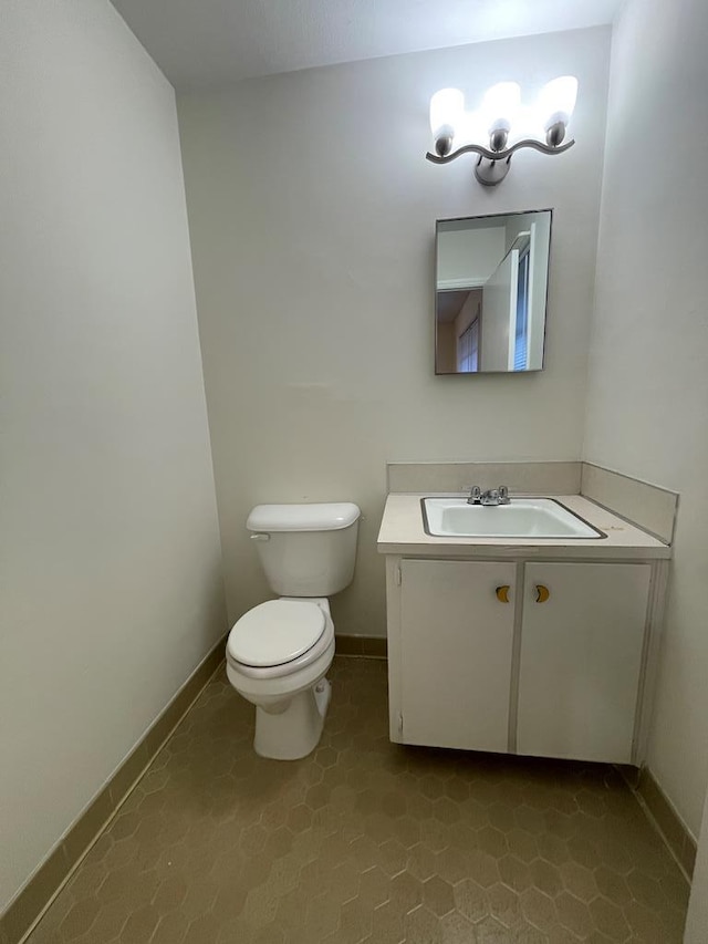 half bathroom with baseboards, toilet, and vanity