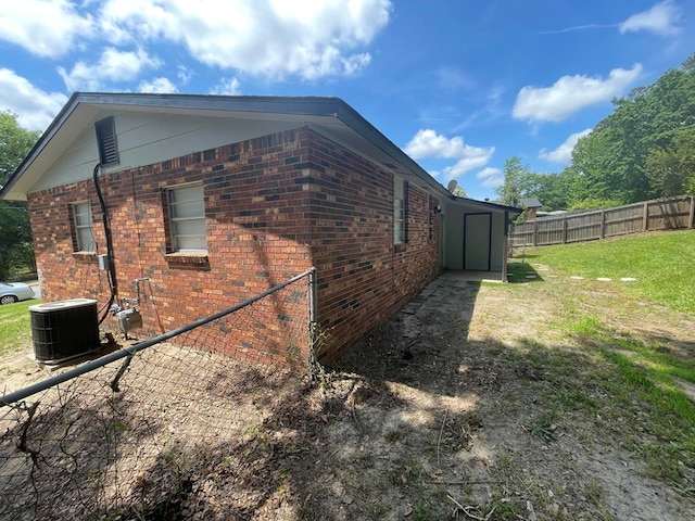 view of side of property featuring a lawn, fence, brick siding, and central AC