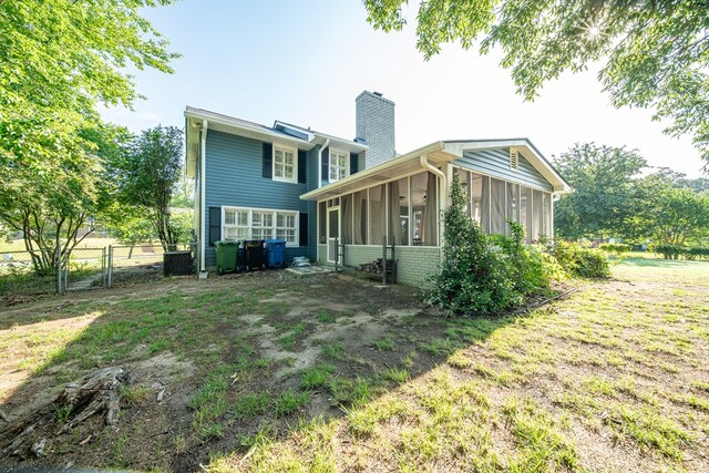 back of house with a chimney, a sunroom, a gate, and brick siding