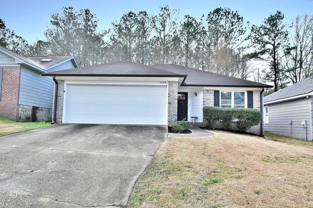single story home featuring brick siding, an attached garage, a front yard, and driveway