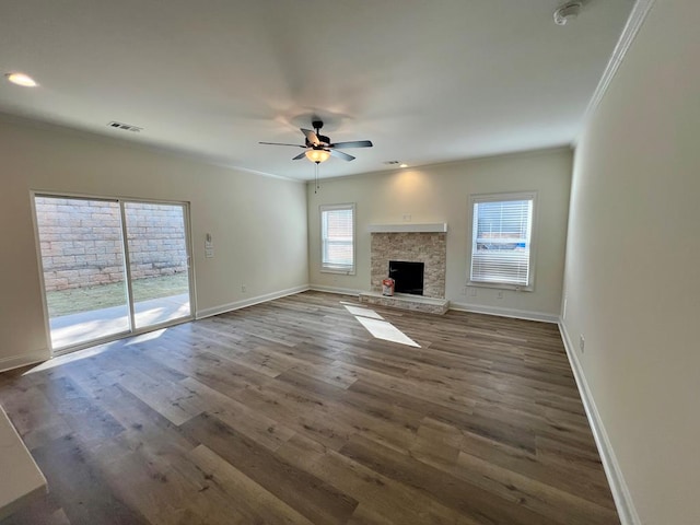 unfurnished living room featuring ornamental molding, a stone fireplace, dark wood-type flooring, and ceiling fan